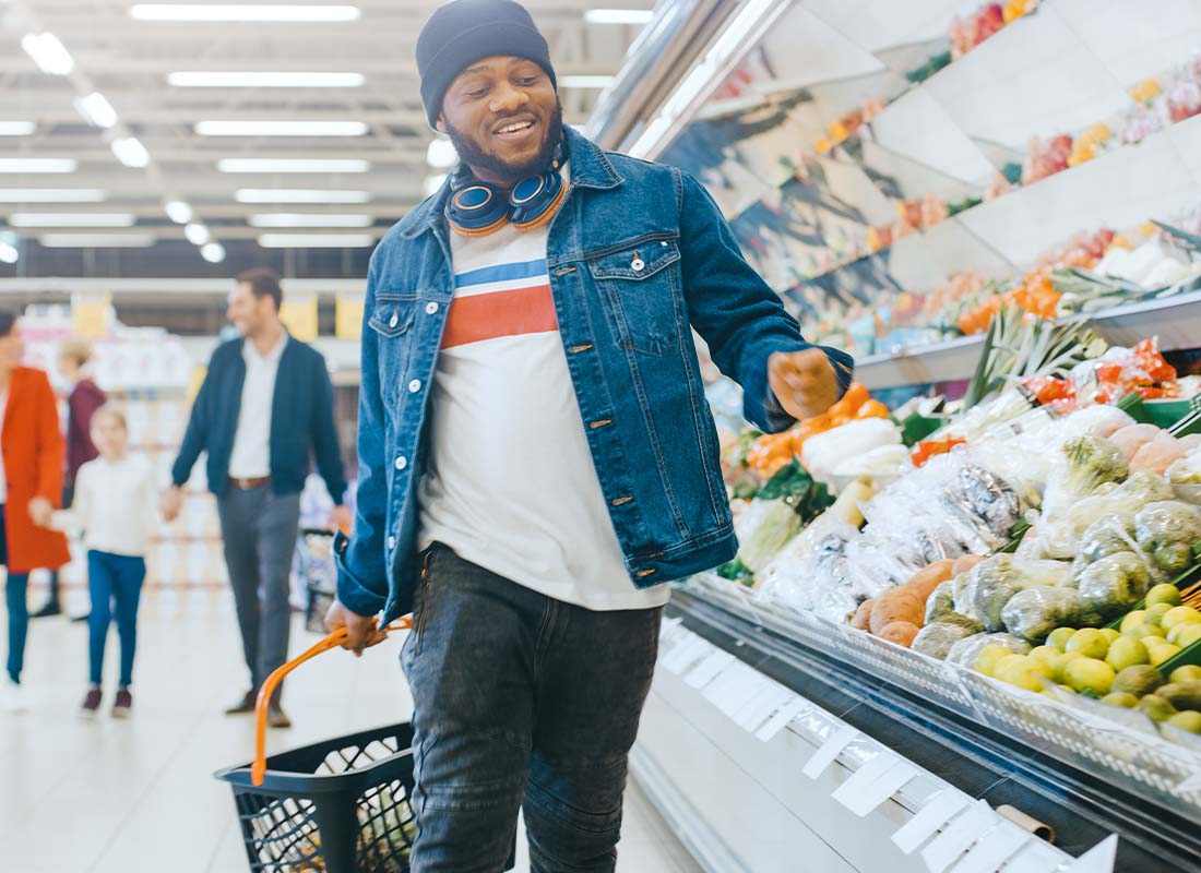 Grocery Store Insurance - Happy Man Shopping With Grocery Basket and Walking Through Fresh Produce Section of the Store