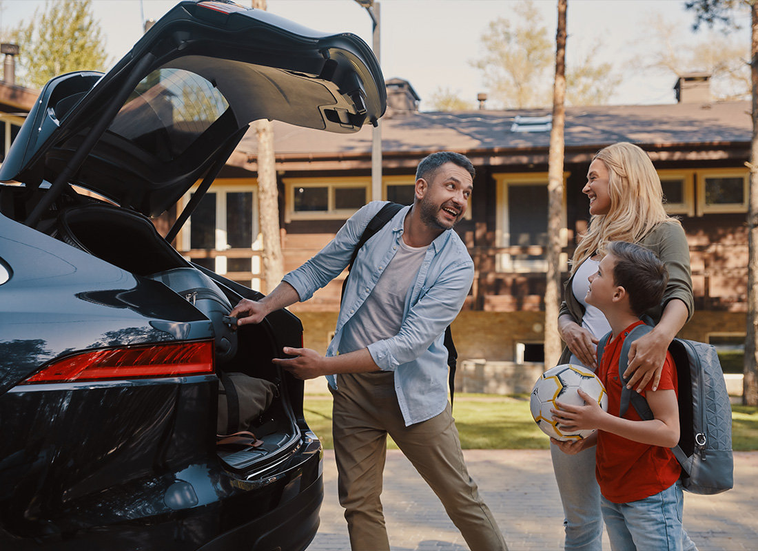 Insurance Solutions - Happy Young Family Packing Stuff Into the Car and Smiling While Standing Near a House